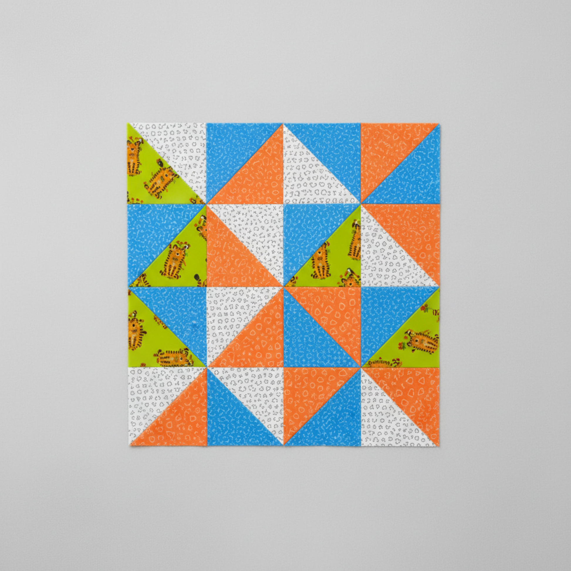 Safari Fun pinwheel quilt block in progress featuring Floating Triangles Blue, Floating Triangles Orange, Tiger Too Lime, and white triangle print by Terry Runyan for Benartex — fabric strips, cut squares, and a rotary cutter shown. Quilts shown for inspiration. Coordinating fabrics and quilt patterns are available at IraRobi Quilts.