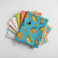 Safari Fun Playful Safari Blue/Multi by Terry Runyan for Benartex shown in a coordinating fabric stack with prints in orange triangles, lime green, coral sorbet, white/black triangles, and multicolor stripe. Quilt blocks shown for inspiration. Coordinating fabrics and quilt patterns are available at IraRobi Quilts.