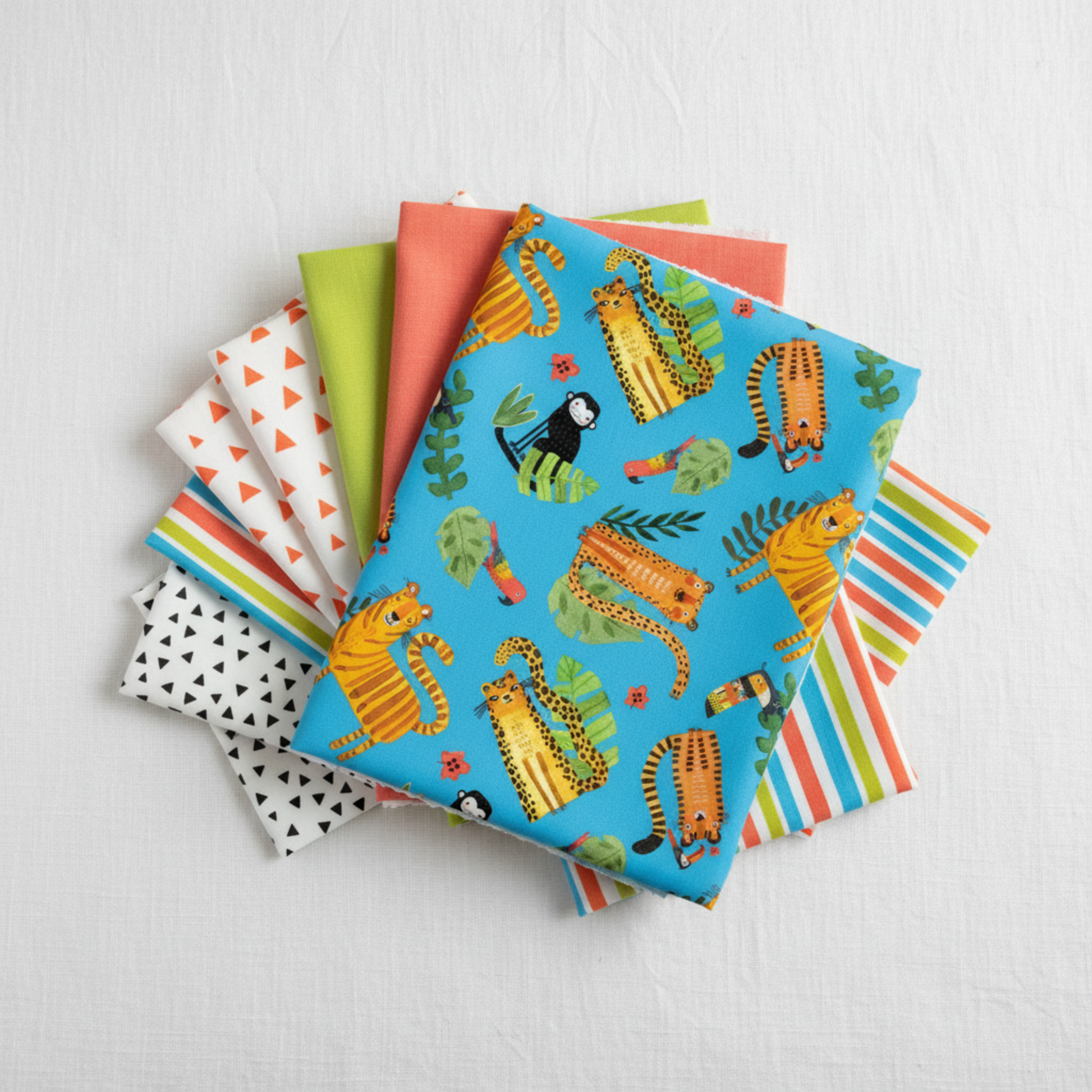 Safari Fun Playful Safari Blue/Multi by Terry Runyan for Benartex shown in a coordinating fabric stack with prints in orange triangles, lime green, coral sorbet, white/black triangles, and multicolor stripe. Quilt blocks shown for inspiration. Coordinating fabrics and quilt patterns are available at IraRobi Quilts.