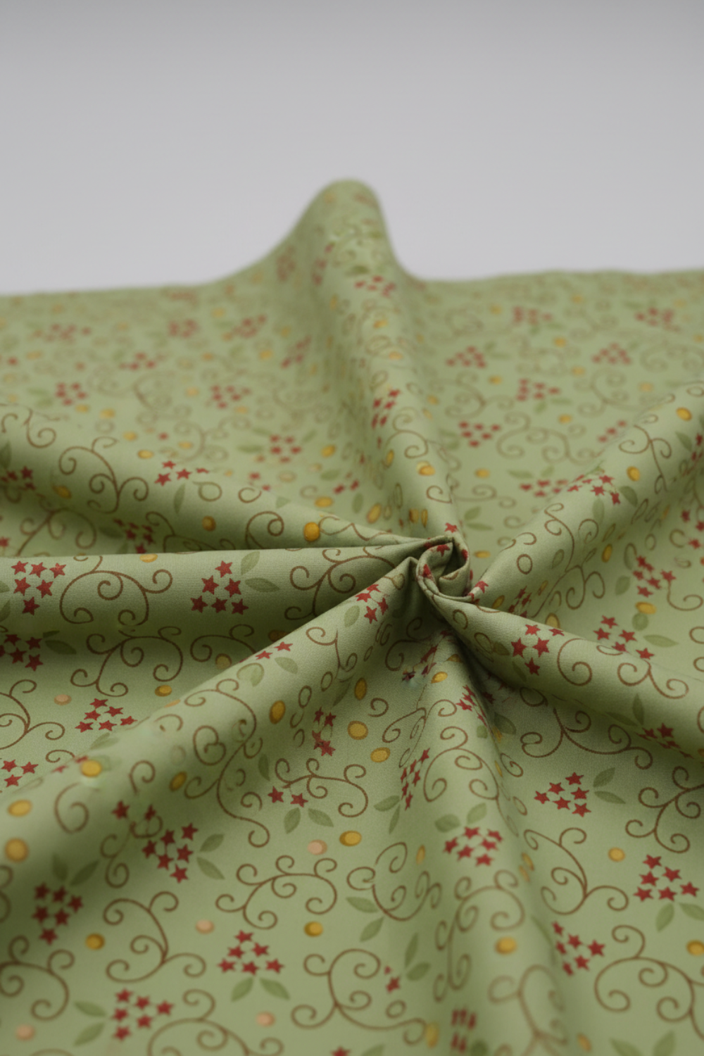 Scraps of Kindness quilting cotton in soft natural folds close-up — aqua with curling vine and red star clusters, emphasizing fabric drape and texture, by Kim Diehl for Henry Glass