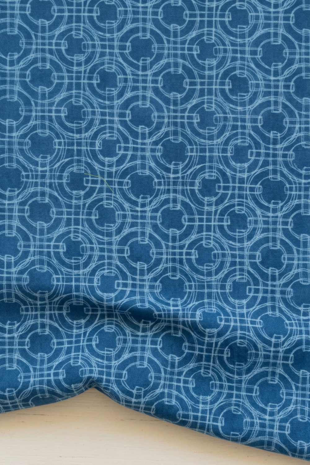 Serena Shores Coastal fabric by Robin Pickens for Moda Fabrics, softly draped with folds along the lower edge, showing pale blue linked rings on a deep blue ground.