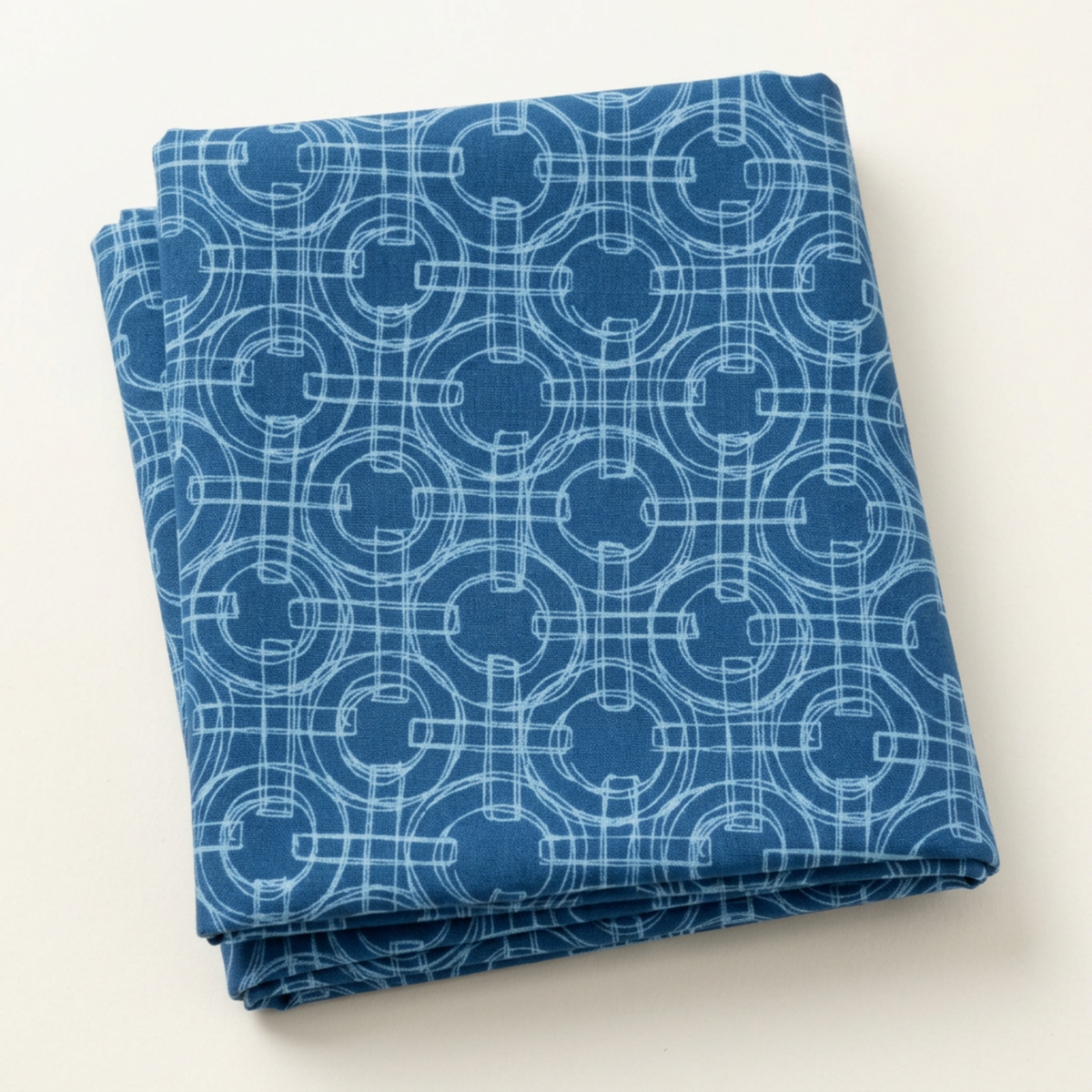 Folded Serena Shores Coastal fabric by Robin Pickens for Moda Fabrics, featuring pale blue linked rings and intersecting lines on deep blue cotton.