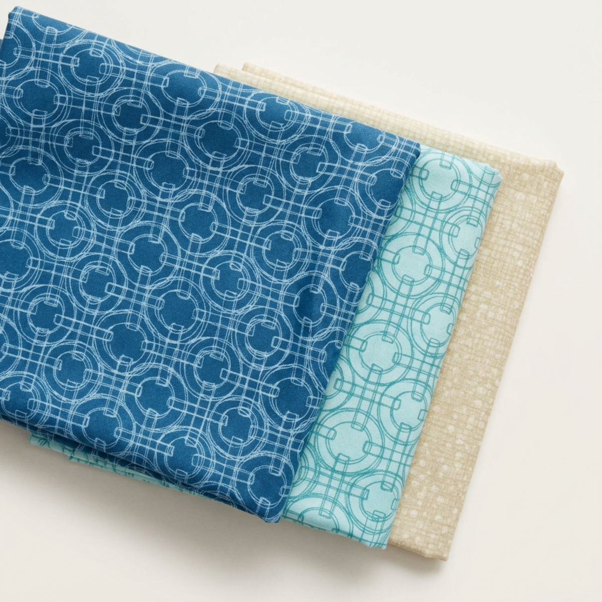 Folded Serena Shores Coastal and Mist fabrics by Robin Pickens for Moda Fabrics, showing linked-ring prints in deep blue and pale aqua with a coordinating cream textured fabric.