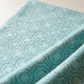 Close-up of Serena Shores Mist fabric by Robin Pickens for Moda Fabrics, softly draped in diagonal folds showing muted teal sketched linked rings on pale aqua cotton.