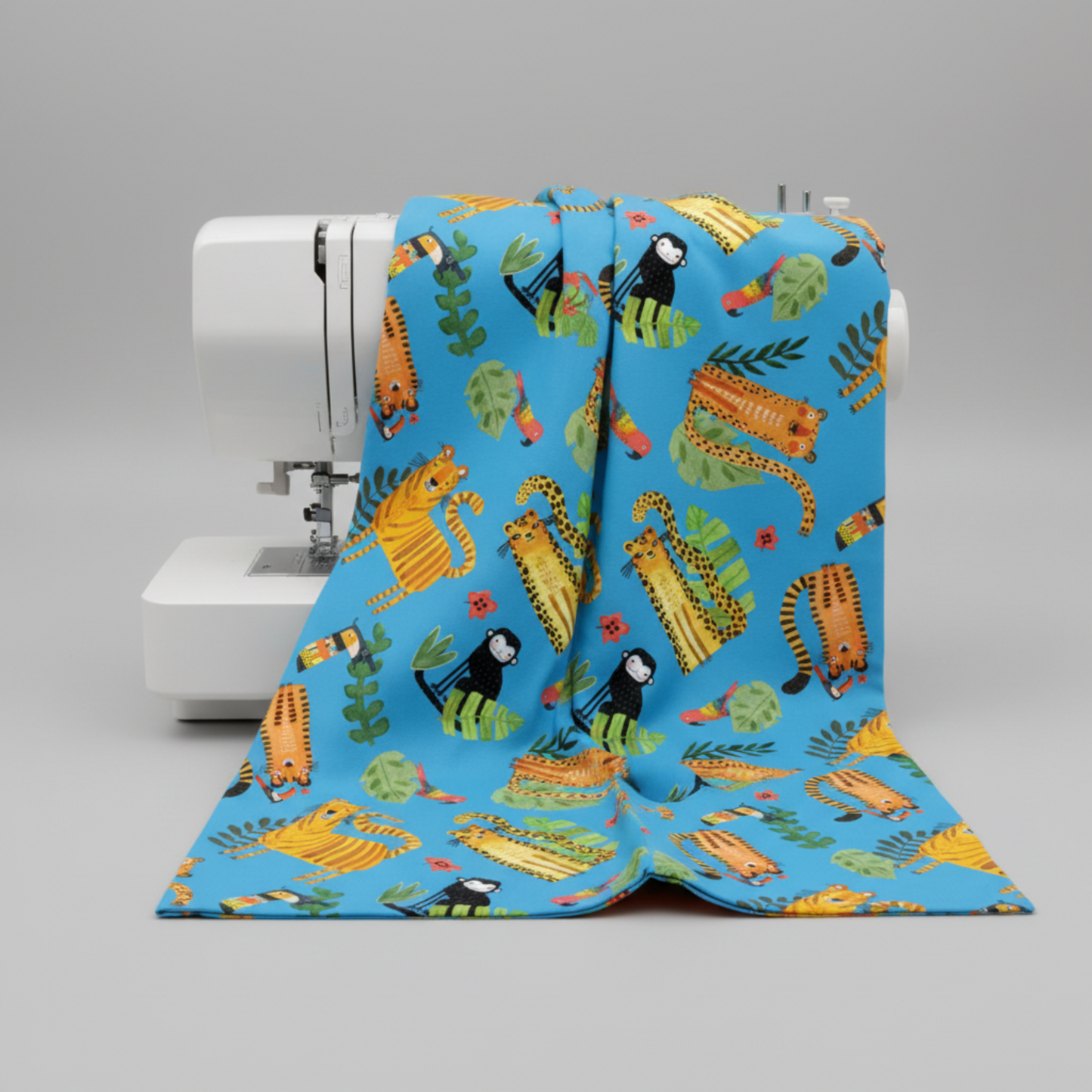 Bright sky blue quilting cotton with whimsical illustrated jungle animals draped over a modern white sewing machine — Safari Fun Playful Safari Blue by Terry Runyan for Benartex