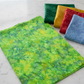 Expressions Batiks Hand-Dyes Shamrock fabric by Riley Blake Designs folded on a white marble surface with coordinating forest green, tomato red, curry yellow, and periwinkle blue tonal batik fabric pieces nearby – bright electric lime-green hand-dyed batik with lively chartreuse yellow and soft teal-blue organic mottled overlays, a fresh high-energy tonal blender perfect for nature-inspired and jewel-tone quilts, 100% cotton batik