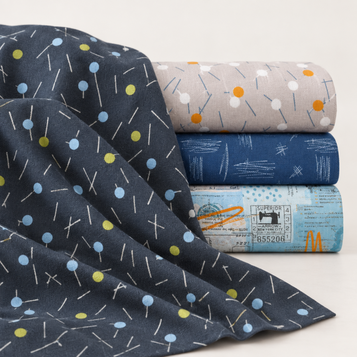 Bluish Pins & Buttons Charcoal fabric draped beside coordinating gray, navy, and pale blue modern quilting fabrics.