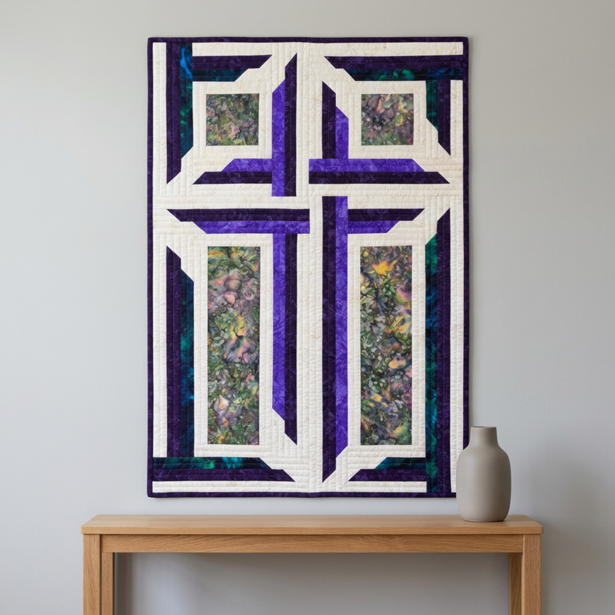 The Wondrous Cross handmade wall quilt displayed on a light-grey wall above an oak console with a neutral ceramic vase.