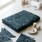 Folded Terrazzo Smoky Teal batik fabric by Riley Blake Designs on a sunlit sewing table with matching triangular fabric pieces, thread spools, pins, and a thimble.