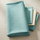 Spotted Dusty Teal fabric by Zen Chic for Moda Fabrics draped and folded on a warm linen surface with coordinating teal, cream, and aqua fabrics – medium teal-blue tonal speckled near-solid blender, perfect for quilt backgrounds, sashing, and borders, 100% cotton