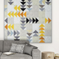 Modern Spotted Geese quilt in deep charcoal, grey, gold and orange Interwoven geometric fabric on a light background, hung above a grey sofa in a Scandinavian living room – Spotted Geese quilt pattern by Zen Chic made with Interwoven Dark Slate, Slate, Butterscotch and Pumpkin fabrics by Jason Yenter. Shop Interwoven Dark Slate at IraRobi Quilts | #flyinggeese #modernquilt #zenchic #interwovenfabric #darkfabric