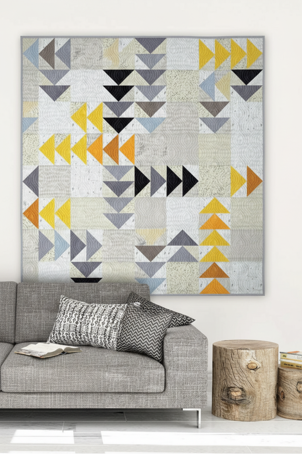Modern Spotted Geese quilt in deep charcoal, grey, gold and orange Interwoven geometric fabric on a light background, hung above a grey sofa in a Scandinavian living room – Spotted Geese quilt pattern by Zen Chic made with Interwoven Dark Slate, Slate, Butterscotch and Pumpkin fabrics by Jason Yenter. Shop Interwoven Dark Slate at IraRobi Quilts | #flyinggeese #modernquilt #zenchic #interwovenfabric #darkfabric