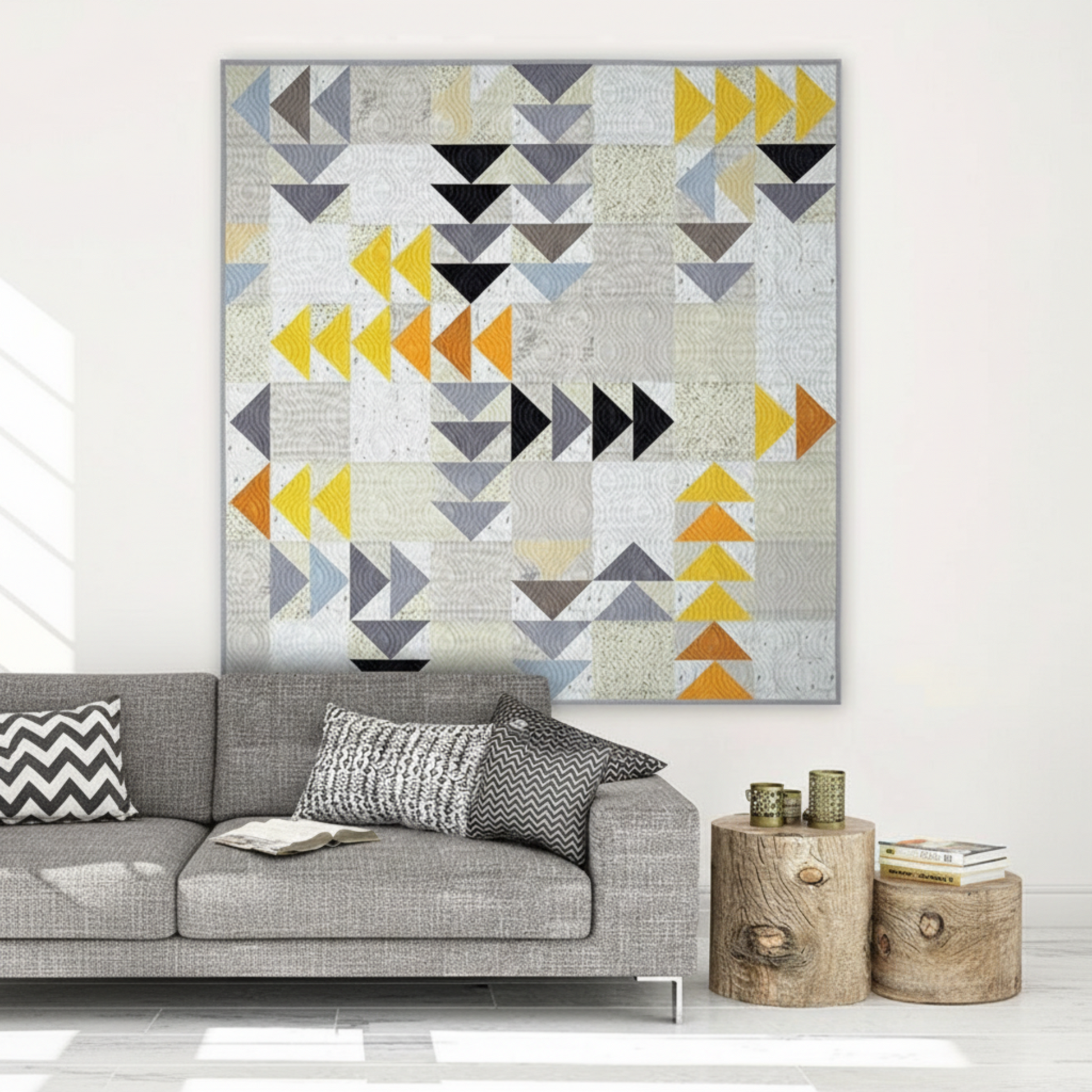Spotted Geese flying geese quilt made with Interwoven Dark Slate as near-black geese, Slate as grey geese, Butterscotch and Pumpkin as gold and orange geese on a light background, hung above a grey sofa in a modern Scandinavian living room – Interwoven Dark Slate fabric by Jason Yenter for In The Beginning Fabrics, available at IraRobi Quilts