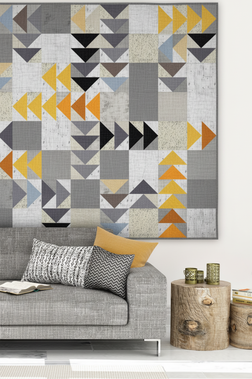 Modern flying geese quilt in cool grey, charcoal, gold and orange Interwoven geometric fabric hung above a grey sofa in a Scandinavian living room – Spotted Geese quilt pattern by Zen Chic made with Interwoven Slate background fabric by Jason Yenter. Shop Interwoven Slate at IraRobi Quilts | #flyinggeese #modernquilt #zenchic #interwovenfabric #quiltingcotton