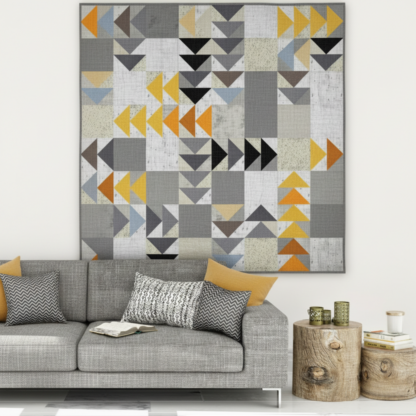 Spotted Geese flying geese quilt made with Interwoven Slate as light background and Charcoal, Espresso, Butterscotch and Pumpkin geese, hung above a grey sofa in a modern Scandinavian living room – Interwoven Slate fabric by Jason Yenter for In The Beginning Fabrics, available at IraRobi Quilts