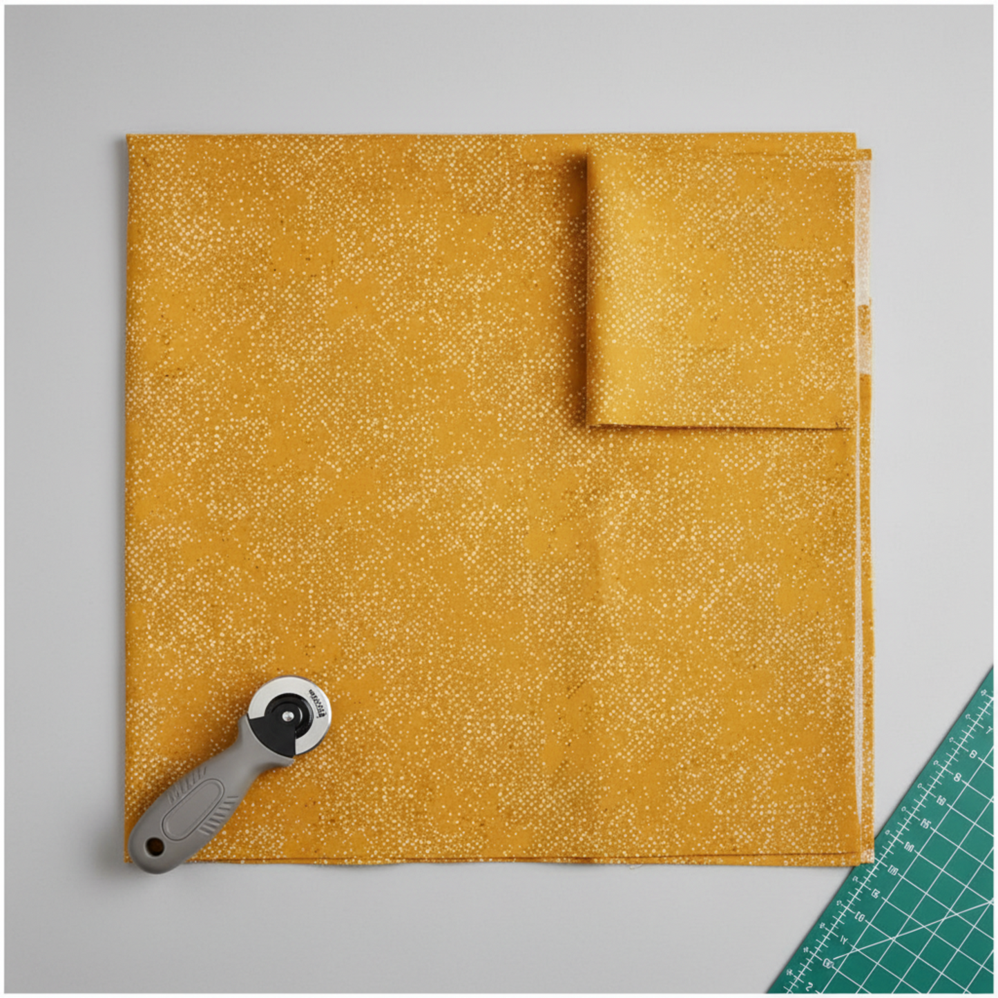 Spotted Sunny golden amber-yellow quilting cotton fabric in a modern quilting workspace – tonal scattered dot blender by Zen Chic for Moda Fabrics, with rotary cutter and cutting mat