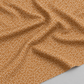 Close-up of Lazy Afternoon Bronze fabric draped in soft folds, showing its small pale dots against the bronze ground.