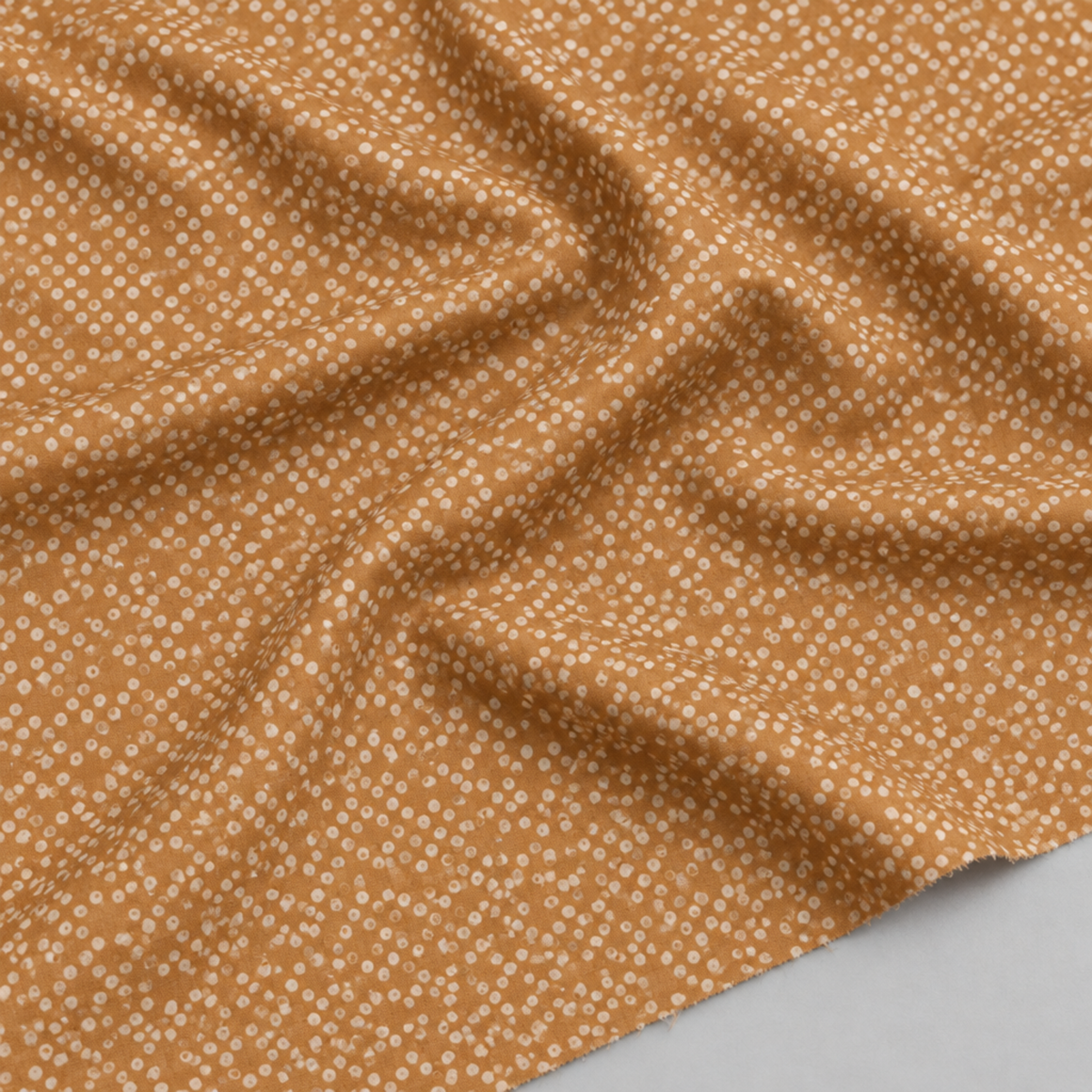 Close-up of Lazy Afternoon Bronze fabric draped in soft folds, showing its small pale dots against the bronze ground.