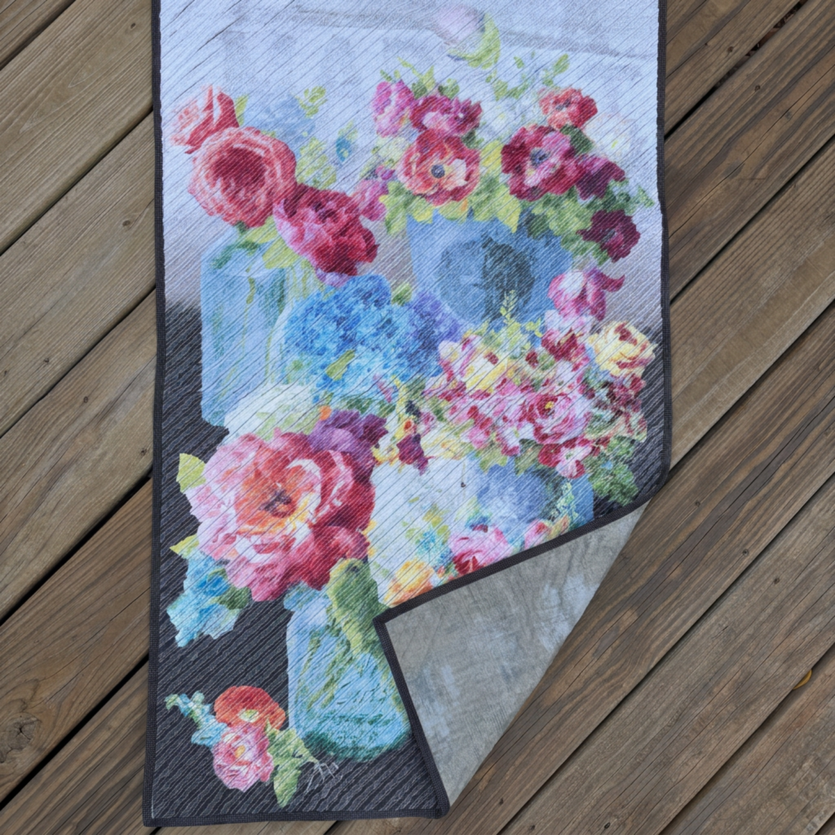 Vase with Flowers wall quilt on wooden decking, with the lower-right corner folded back to reveal pale-grey patterned backing and dark binding.