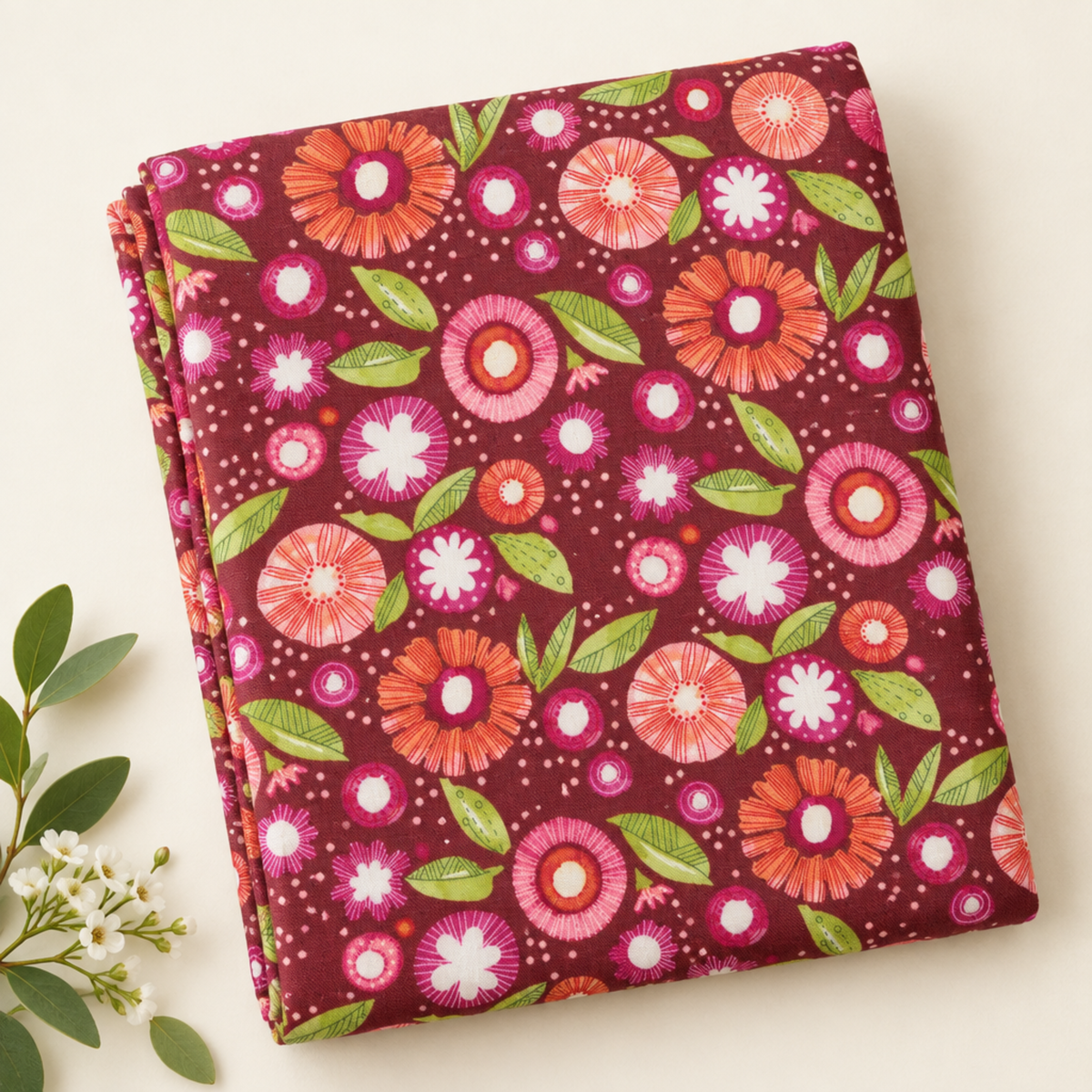 Folded Superbloom Posy Party Zinnia fabric by Robin Pickens for Moda Fabrics, styled on a cream surface beside a sprig of white flowers.
