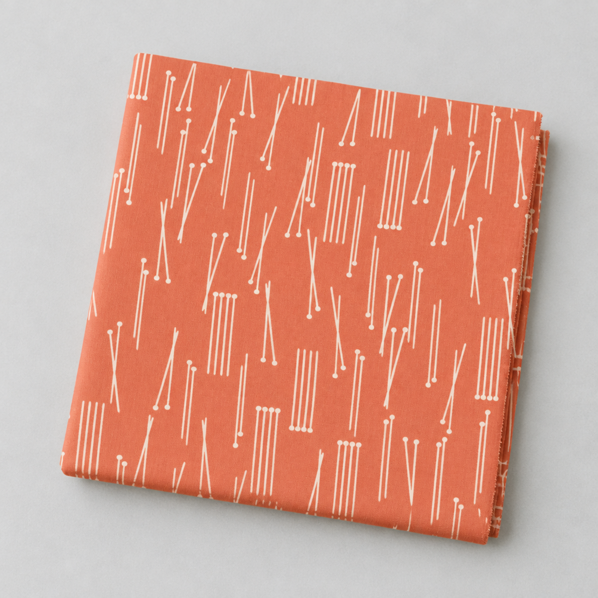 Folded Lazy Afternoon Marmalade fabric showing the fine cream linear print on a coral ground.