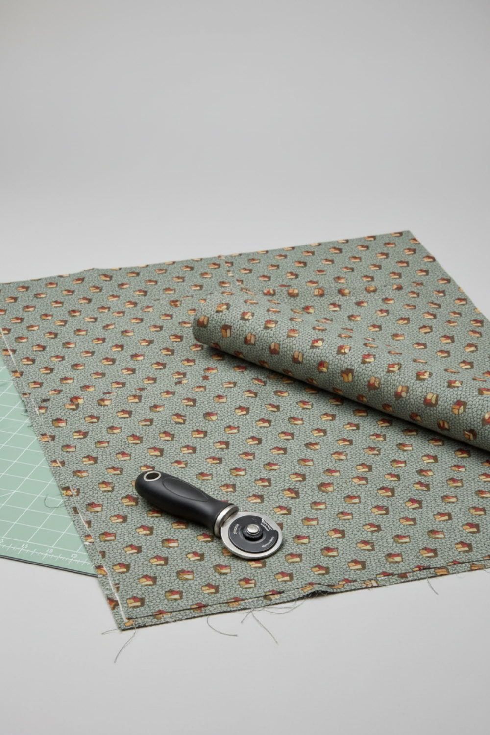 The Fox Homestead Slate Blue Green Tossed Cubes quilting cotton fabric styled in a modern quilting studio with a cutting mat and rotary cutter.