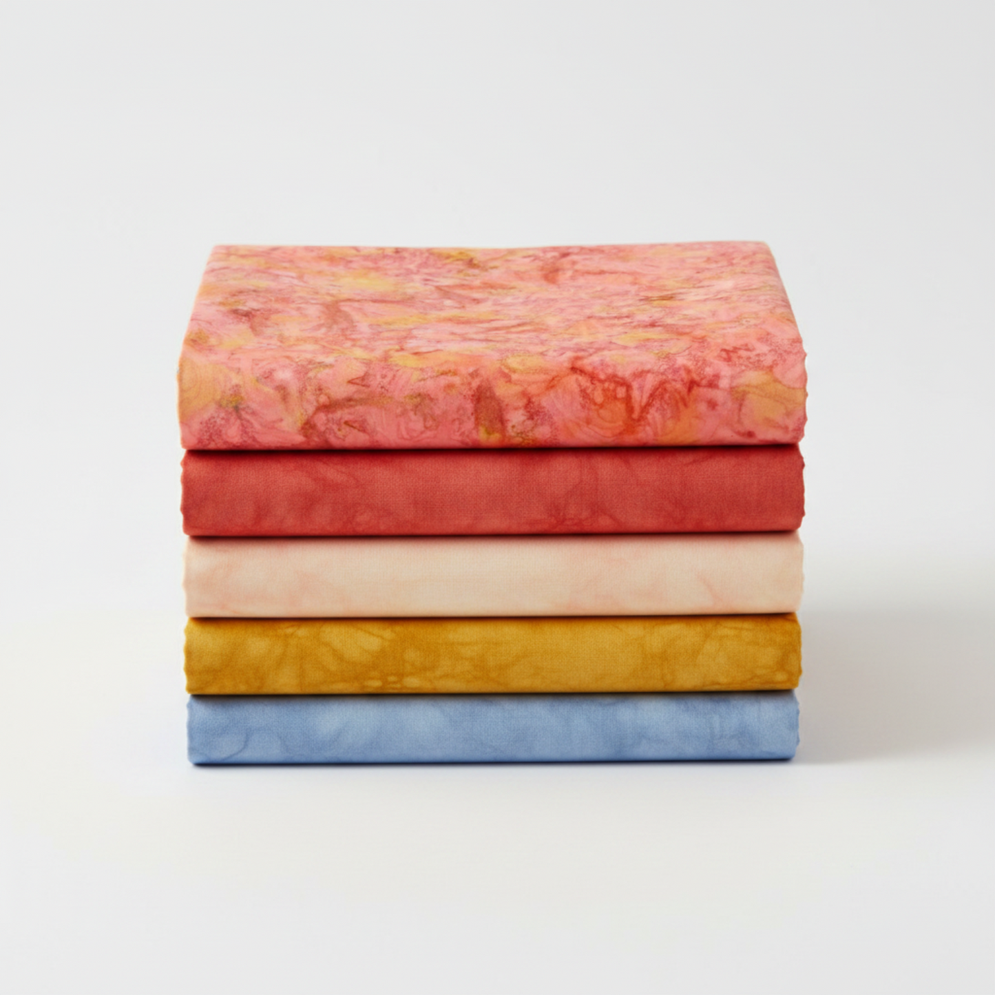 Expressions Batiks Hand-Dyes Sunset fabric by Riley Blake Designs on top of a coordinating stack of five tonal batik fabrics – soft coral-pink on top with tomato red, soft peach-cream, curry yellow, and periwinkle blue tonal batiks below, 100% cotton
