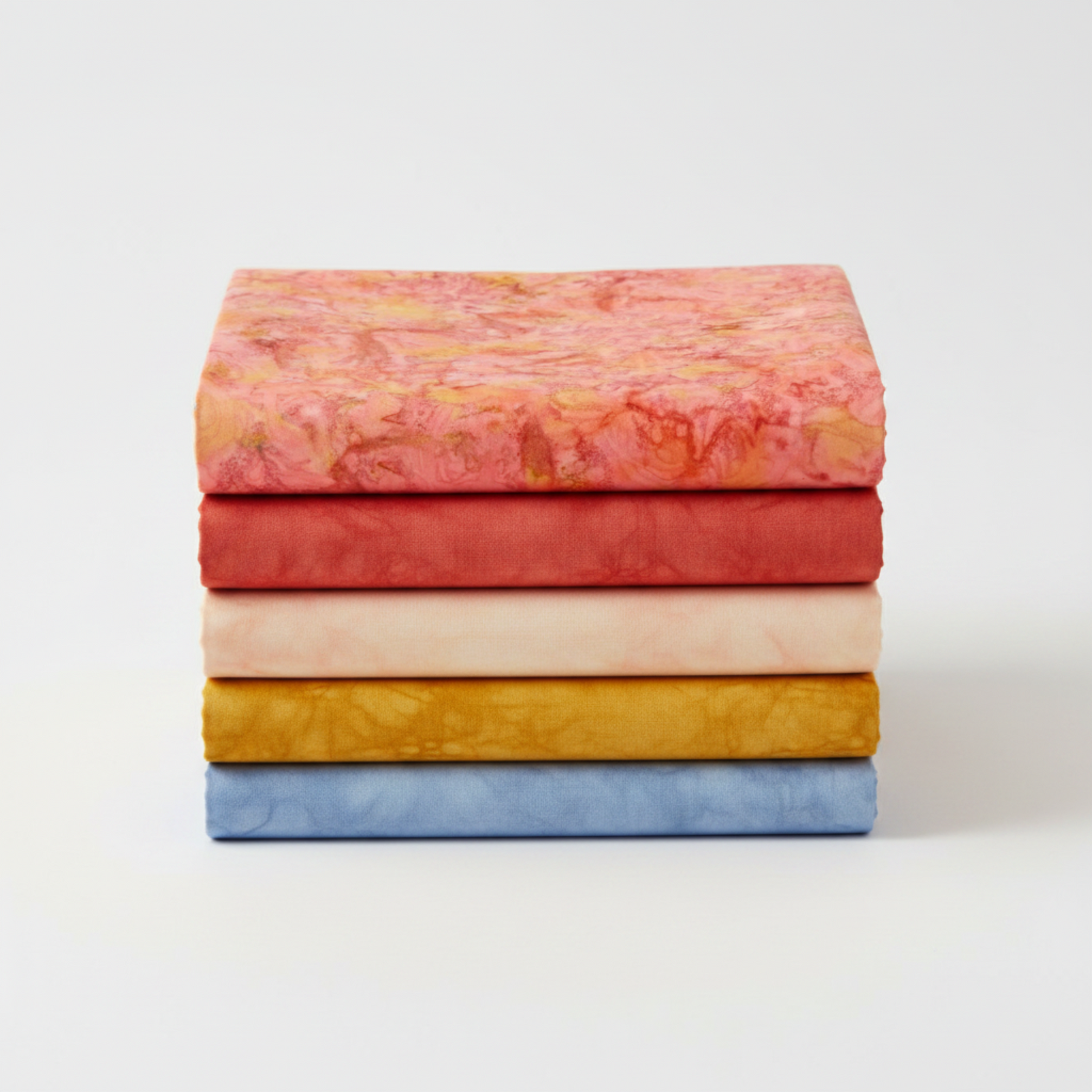 Expressions Batiks Hand-Dyes Sunset fabric by Riley Blake Designs on top of a coordinating stack of five tonal batik fabrics – soft coral-pink on top with tomato red, soft peach-cream, curry yellow, and periwinkle blue tonal batiks below, 100% cotton