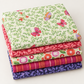 Coordinating Superbloom fabrics by Robin Pickens for Moda Fabrics, neatly stacked to showcase butterfly, leafy, floral, and stripe prints in cream, coral, pink, and indigo.