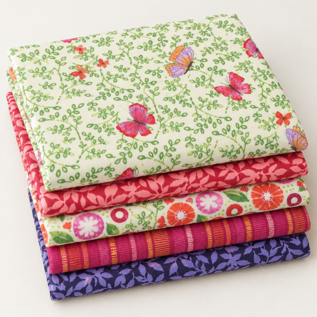 Coordinating Superbloom fabrics by Robin Pickens for Moda Fabrics, neatly stacked to showcase butterfly, leafy, floral, and stripe prints in cream, coral, pink, and indigo.