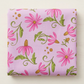 Folded Superbloom Daisyish Freesia fabric by Robin Pickens for Moda Fabrics on a light surface, showing pink flowers, golden-brown centers, and green leaves on lavender-pink cotton.