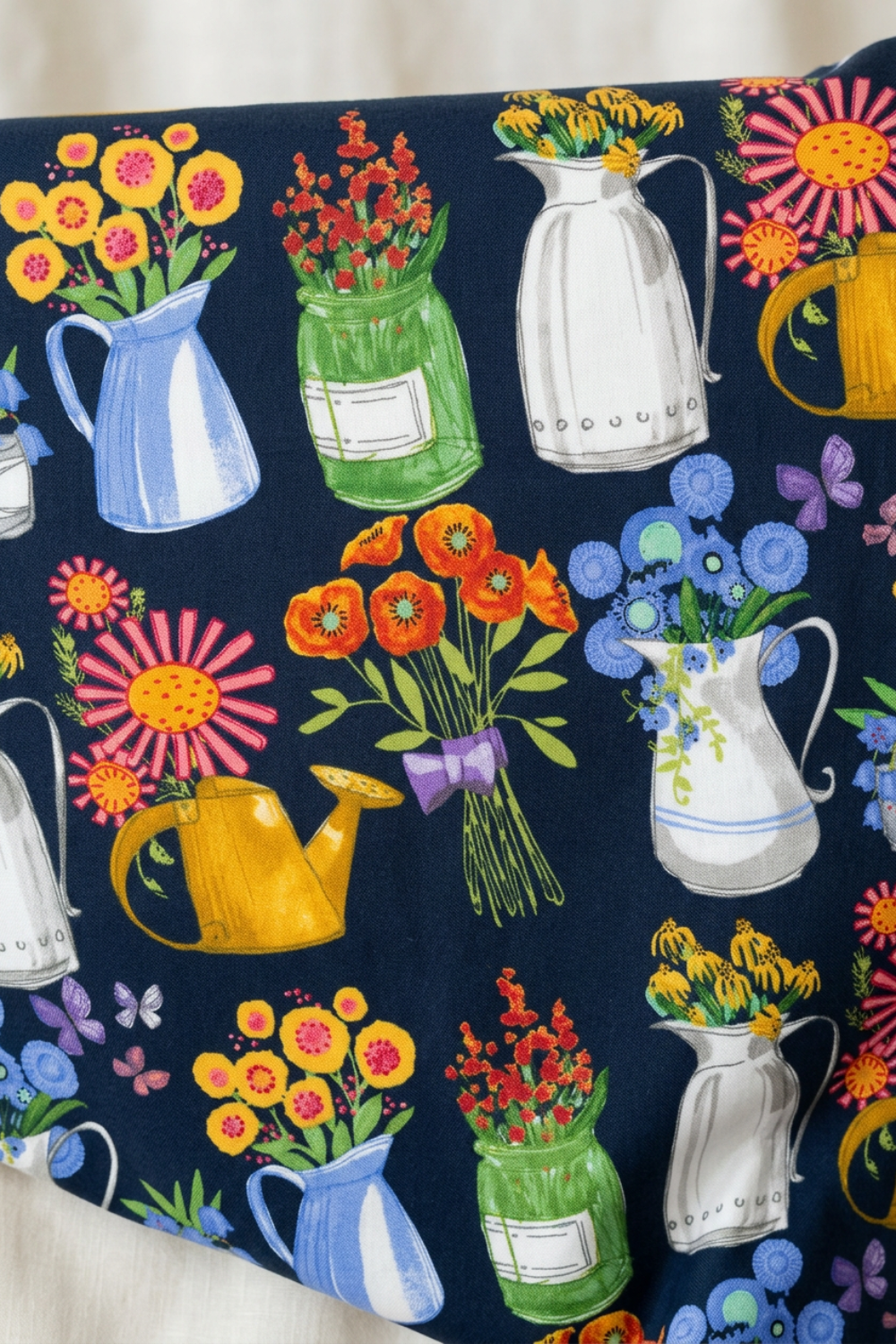 Superbloom Flea Market Vases Indigo fabric by Robin Pickens for Moda Fabrics, draped across a light surface to display colorful floral pitchers, green jars, yellow watering cans, and bouquets.