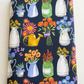 Neatly folded Superbloom Flea Market Vases Indigo fabric by Robin Pickens for Moda Fabrics on a light tabletop, showing colorful flower-filled containers and butterflies on dark indigo cotton.