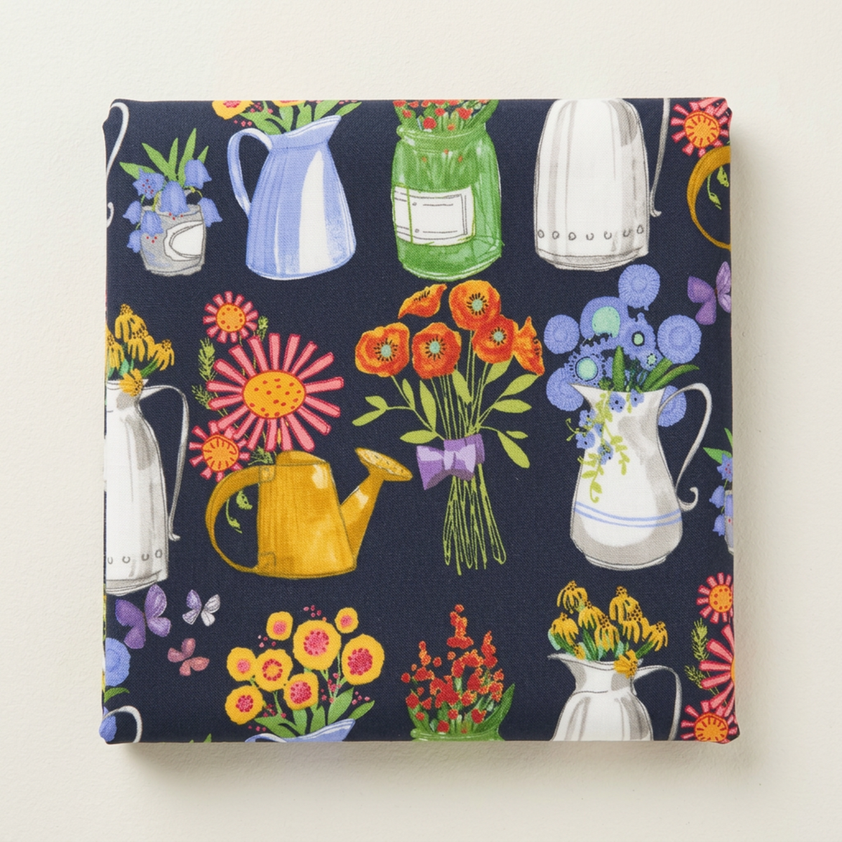 Folded Superbloom Flea Market Vases Indigo fabric by Robin Pickens for Moda Fabrics on a light surface, showing colorful flower-filled pitchers, jars, and watering cans on dark indigo cotton.