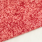 Close-up of Superbloom Leafy Geranium fabric by Robin Pickens for Moda Fabrics, showing coral-pink leaves on rich red cotton with a diagonal fabric edge against a light surface.