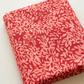 Superbloom Leafy Geranium fabric by Robin Pickens for Moda Fabrics, neatly folded at an angle on a light tabletop, showing coral-pink leaves on geranium-red cotton.