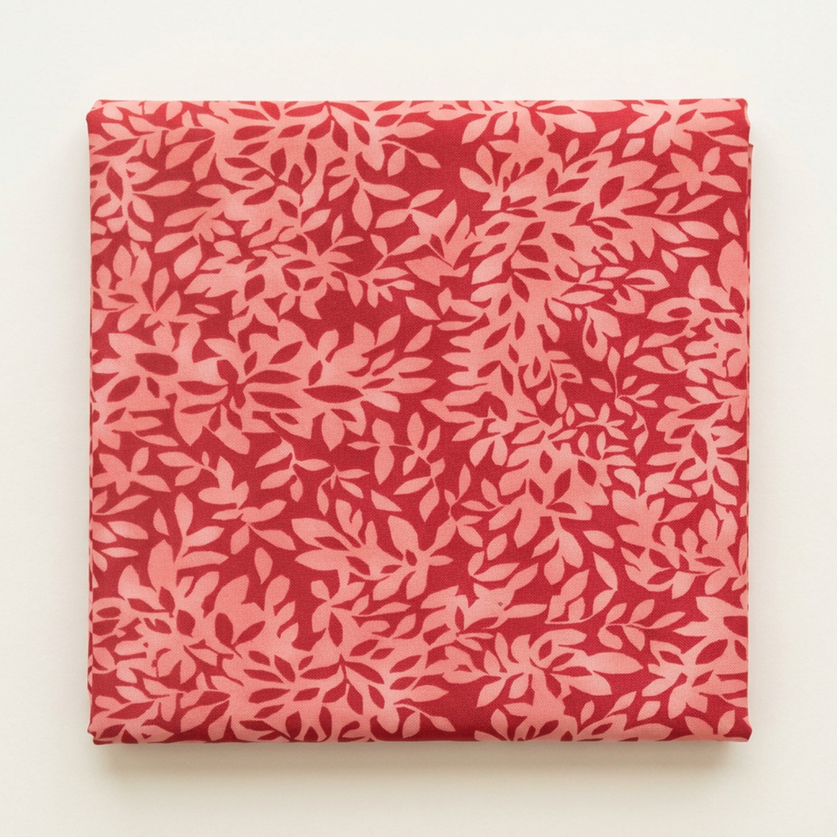 Folded Superbloom Leafy Geranium fabric by Robin Pickens for Moda Fabrics on a light surface, showing coral-pink leafy branches on geranium-red cotton.