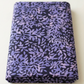 Neatly folded Superbloom Leafy Indigo fabric by Robin Pickens for Moda Fabrics on a light tabletop, showing lavender-purple leaves on dark indigo cotton.