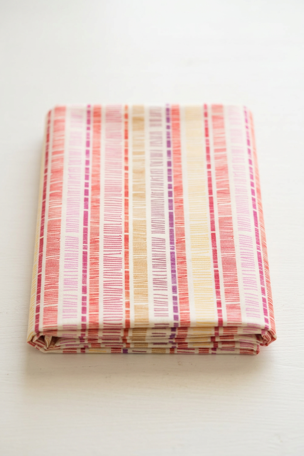 Superbloom Scribble Stripe Cream fabric by Robin Pickens for Moda Fabrics, neatly folded on a light tabletop with colorful vertical scribble-stripe bands on cream cotton.