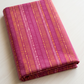 Superbloom Scribble Stripe Orchid fabric by Robin Pickens for Moda Fabrics, neatly folded on a light tabletop with golden-orange and pink stripe bands on orchid-magenta cotton.