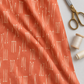 Lazy Afternoon Marmalade fabric draped beside scissors and thread, showing its cream linear print on a coral ground.