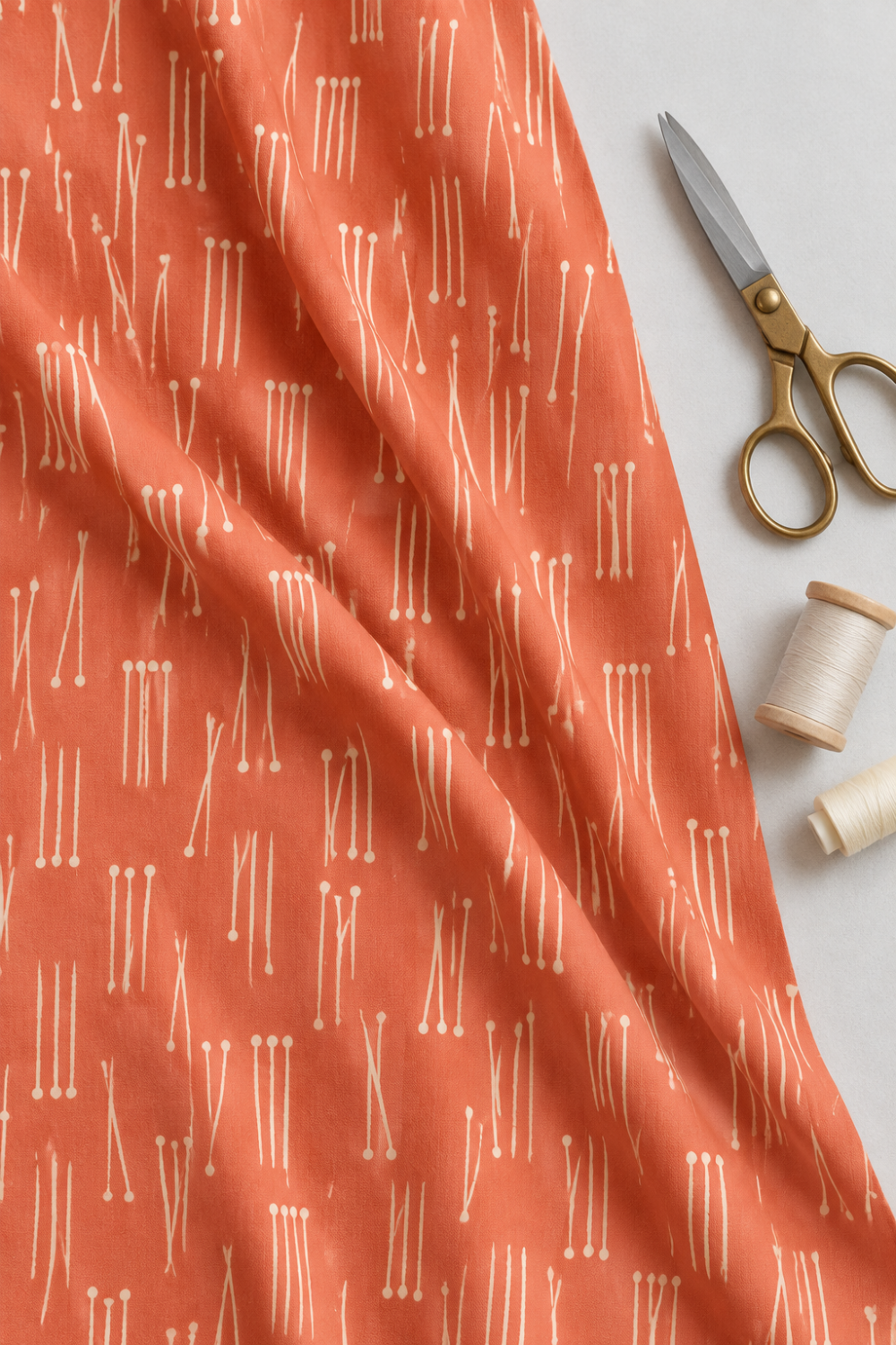 Lazy Afternoon Marmalade fabric draped beside scissors and thread, showing its cream linear print on a coral ground.