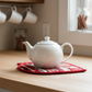 Leaf-Shaped Quilted Hot Pad in Christmas Red under a white teapot – handmade kitchen gift at IraRobi Quilts | #quiltedhome #hotpad #handmadegift