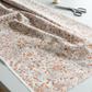 Terrazzo Coastal Path Fabric by Riley Blake Designs draped in soft folds across a light-gray sewing table beside scissors and an ivory thread spool.