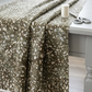 Terrazzo Khaki Fabric by Riley Blake Designs draped over a light-gray sewing table beside scissors and an ivory thread spool.