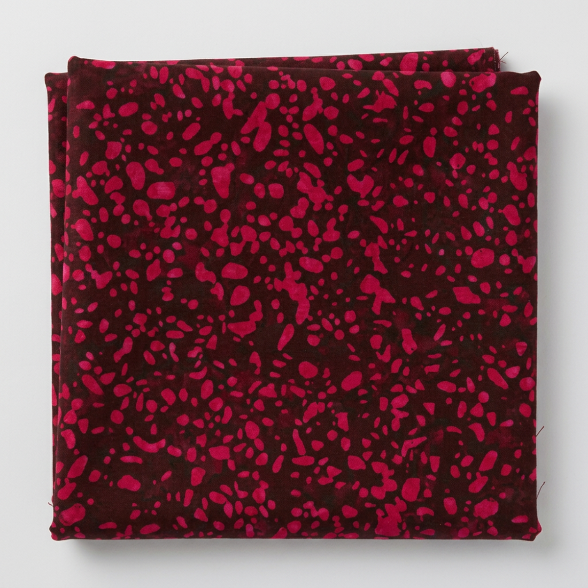Folded Terrazzo Mahogany batik fabric by Riley Blake Designs, showing raspberry-magenta speckles on a deep burgundy ground against a light gray background