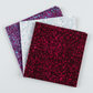 Terrazzo Mahogany batik fabric by Riley Blake Designs fanned in front of coordinating pale blue-gray and aqua-speckled purple fabrics on a light gray background.
