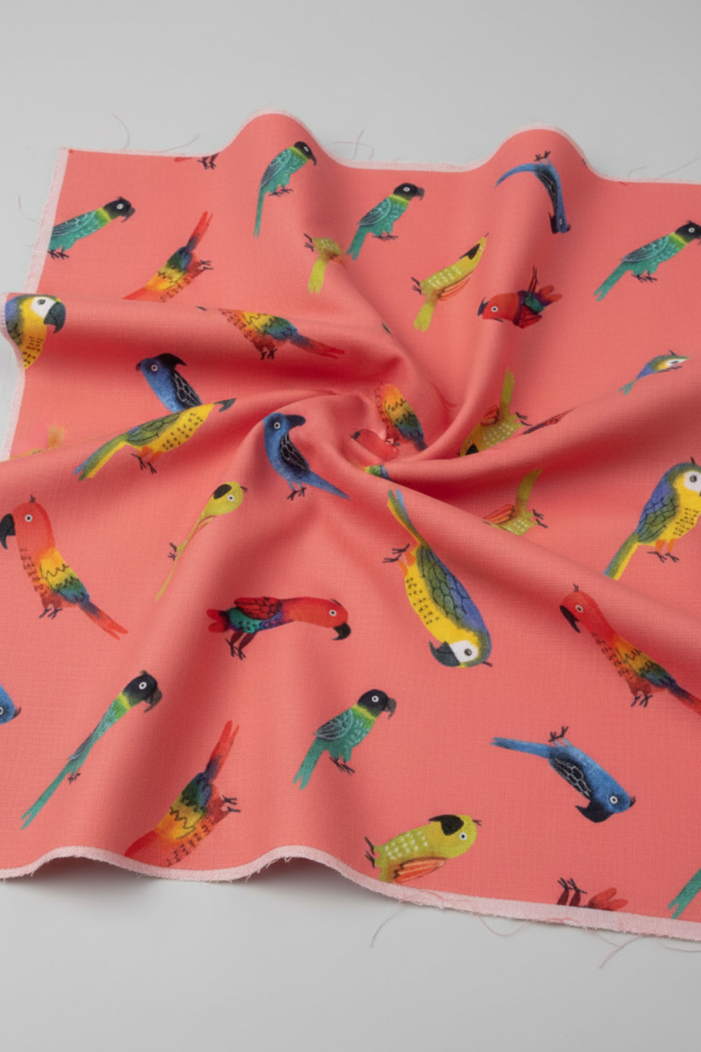 Close-up of coral sorbet pink quilting cotton with colorful tropical parrots in soft folds — Safari Fun Jungle Birds Sorbet by Terry Runyan for Benartex