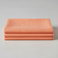 Thatched Coral quilting cotton by Robin Pickens for Moda Fabrics — three folded yards stacked on a grey surface, warm coral near-solid with subtle crosshatch texture