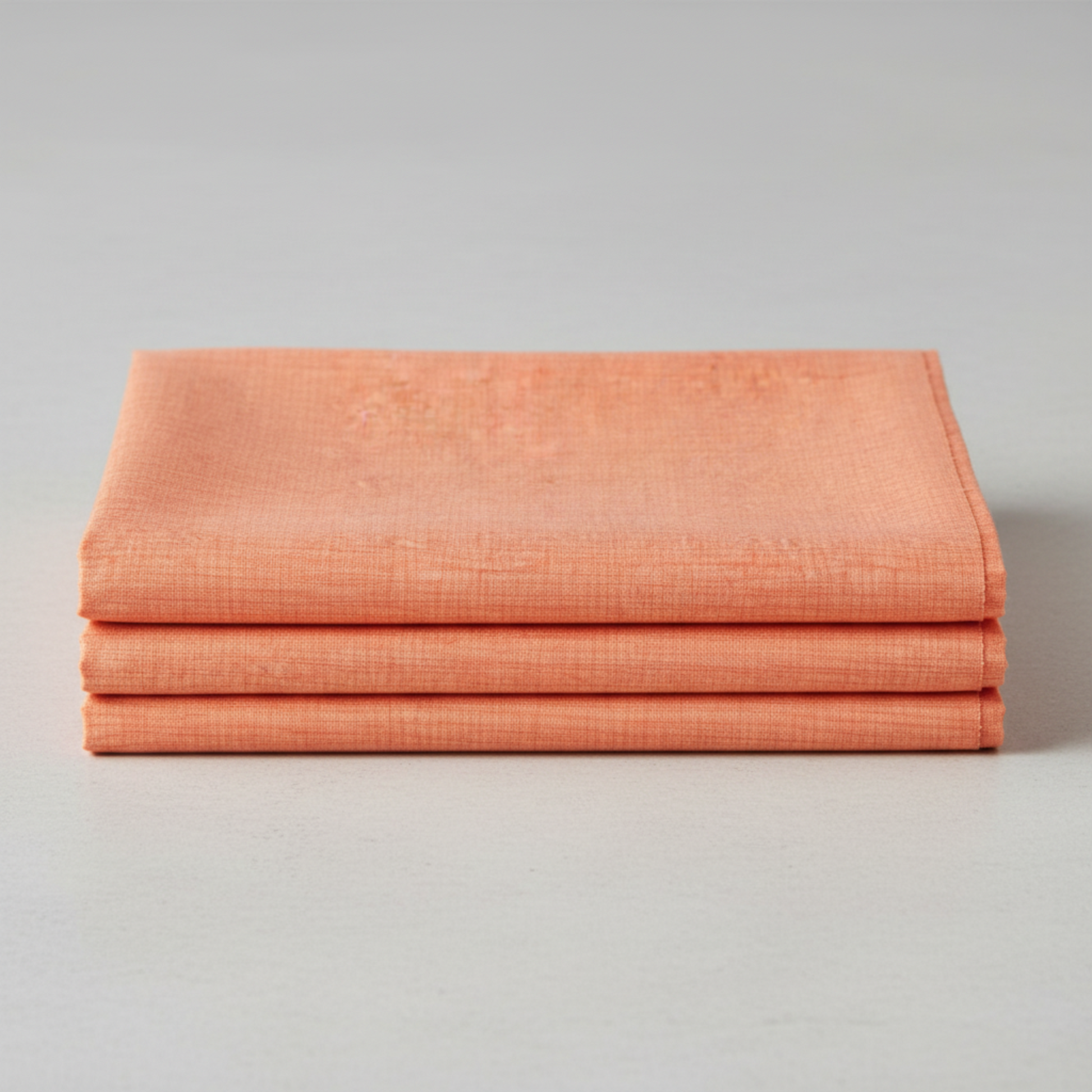 Thatched Coral quilting cotton by Robin Pickens for Moda Fabrics — three folded yards stacked on a grey surface, warm coral near-solid with subtle crosshatch texture